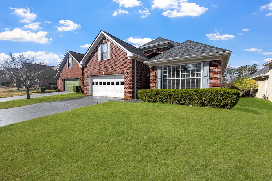 FHA loan requirements outcome: a red-brick suburban starter home with a well-kept lawn under a bright blue sky, the kind of property the FHA loan requirements were written to make accessible for working-class buyers
