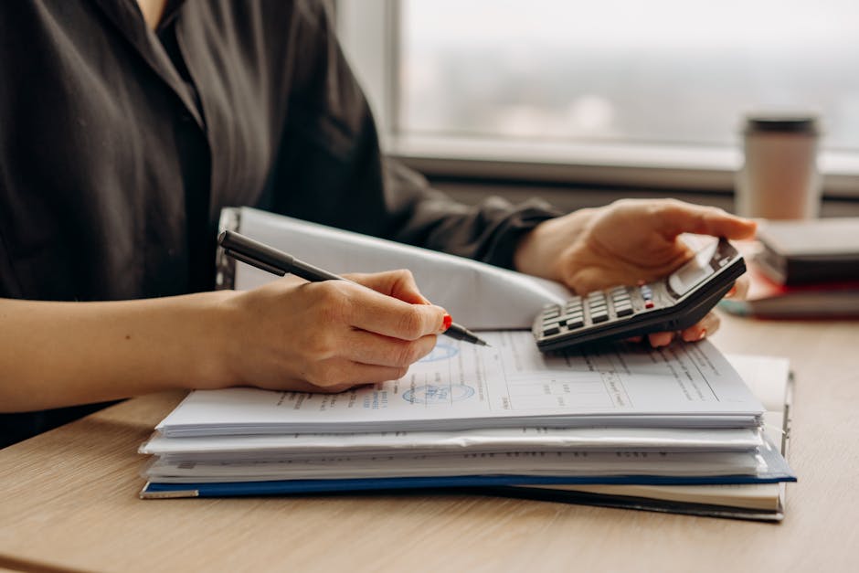 HELOC rates today closing-cost review: a close-up of hands using a calculator with mortgage documents and rate sheets spread across a desk, the practical math step where the first-year all-in cost of competing HELOC rates today gets compared apples-to-apples before any disclosure is signed